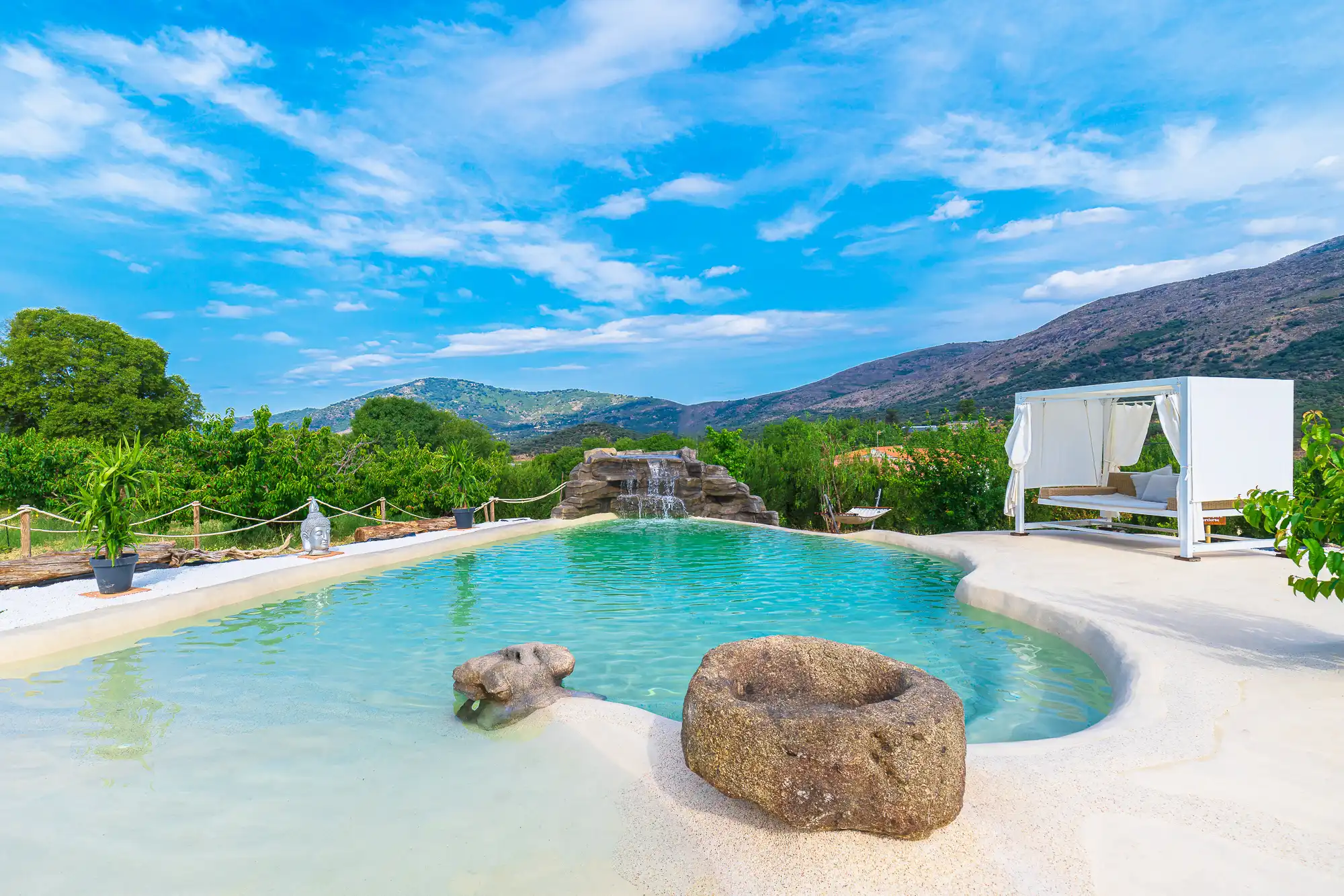La piscina-playa de agua salada con cascada y las montañas del Valle del Jerte al fondo