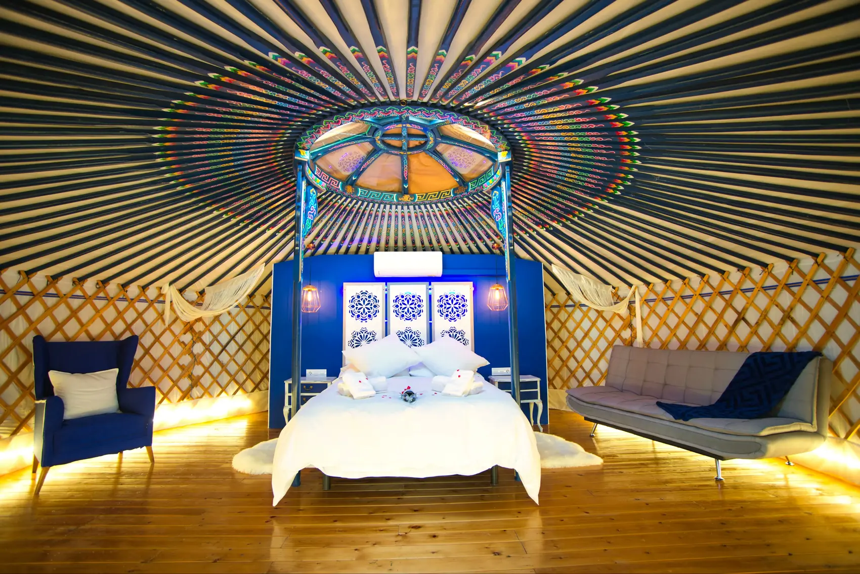 Interior de la Yurta Cielo de frente: la cama con dosel bajo la corona de madera pintada, todo en azul cobalto, con la celosía de madera a los lados
