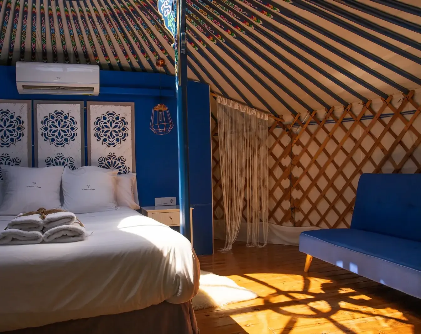 La cama azul cobalto de la Yurta Cielo con el sol de la tarde entrando por la celosía