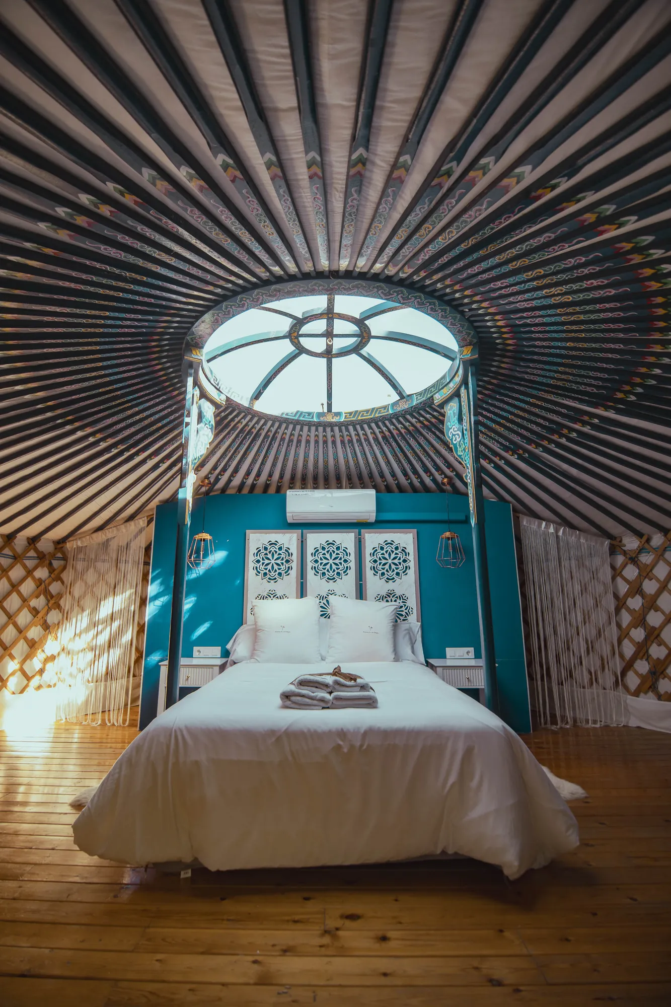 La cama bajo la corona de madera pintada de la yurta, con la luz de la mañana entrando por la cúpula